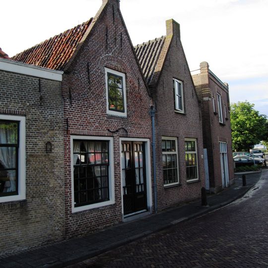 Rechts een pand met puntgevel waarin een zoldervenster met ontlastingsboog. Links een pand met puntgevel, versierd met vlechtingen en geblokte ontlastingsbogen