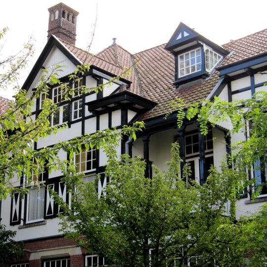 Rechterdeel van een vrijstaand bouwblok bestaande uit twee symmetrische villa's, gebouwd in overgangsarchitectuur, gecombineerd met kenmerken van de 'Stick-style'