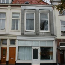 Twee panden met verminkte bakstenen gevels met rechte kroonlijst. De verdieping voorzien van Dorische pilasterstellingen en fries van metselmozaïek