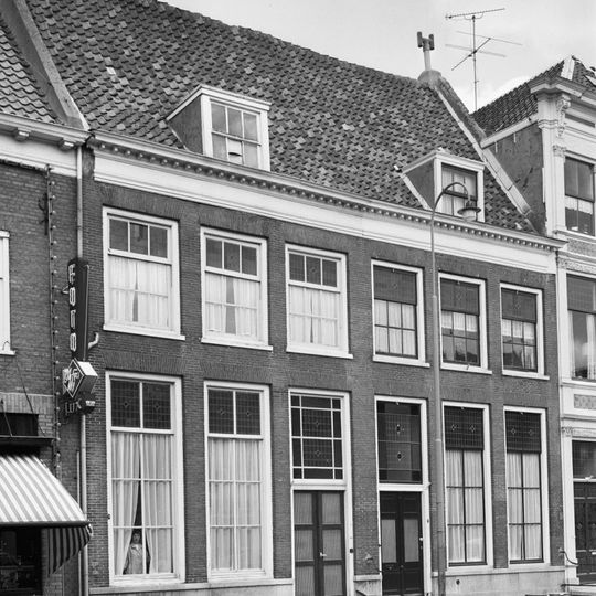 Gedeelte van in oorsprong twee huizen onder een hoog zadeldak tussen puntgevels. De lijstgevel die voor het pand in de eerste helft der 19e eeuw werd opgetrokken heeft een hardstenen plint.