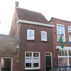 Achter een moderne gevel een huis met dwars zadeldak tussen zijtopgevels