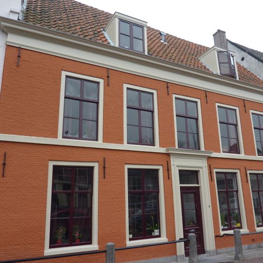 Linker gedeelte van een pand met verdieping en door pannen gedekt zadeldak, evenwijdig aan de straat, links afgesloten door een puntgevel.