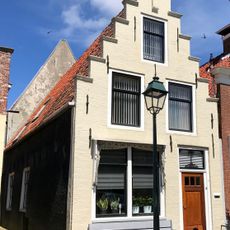 Pand onder zadeldak tegen gepleisterde trapgevel met verhoogd achterhuis tussen twee puntgevels