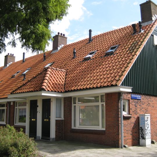 Blok met 8 woningen, gecombineerde toegangen van twee woningen onder een ingestoken schilddak, zijkant met houten topgevel, aan oostkant toegangspoort tot binnenterrein.