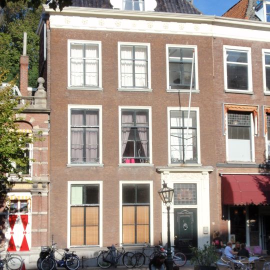 Pand met bakstenen gevel met Dorische kroonlijst. Hardstenen stoep met palen en kettingen, gesneden deur met omlijsting