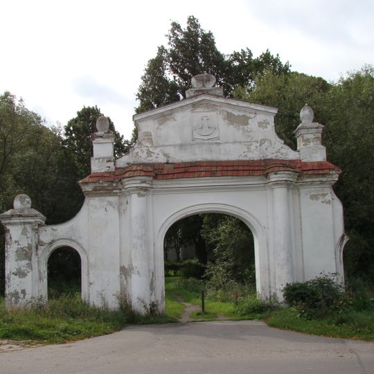 Fragmenty muru oddzielającego dziedziniec pałacu od folwarku z zachowaną z bramą i furtą, brama oddzielona śladami fosy od dziedzińca pałacowego