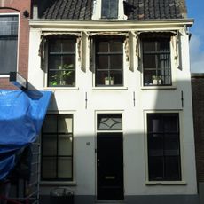 Pand met blauwgepleisterde gevel met rechte kroonlijst onder zadeldak, terzijde in topgevel eindigend met opzet