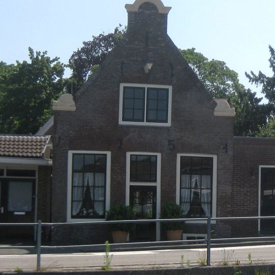 Ten dele houten huis met bakstenen puntgevel, voorzien van een halsje onder gebogen afdekking