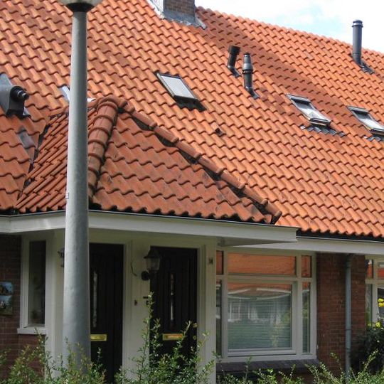 Blok met 8 woningen, gecombineerde toegangen van twee woningen onder een ingestoken schilddak, zijkant met houten topgevel, aan oostkant en westkant toegangspoorten tot binnenterrein.