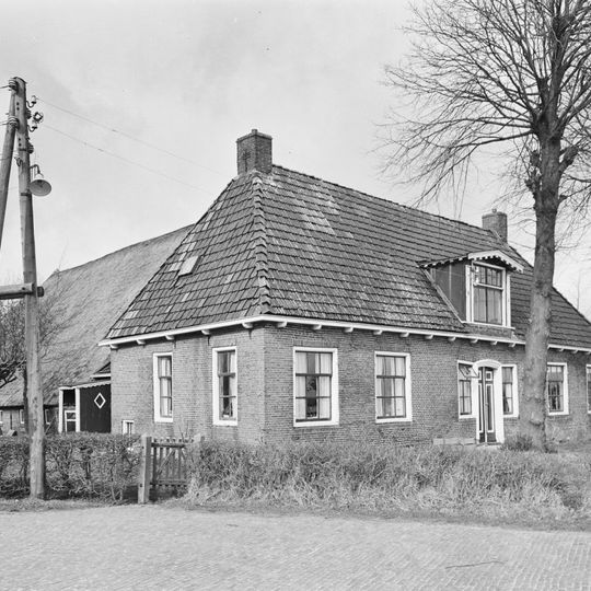 Boerderij met groot dwars gebouwd woonhuis onder schilddak met roedenverdeling in de vensters naast ingang met zijlichten
