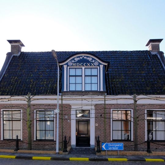 Vijf traveeën breed huis met omlijste ingang met aanzetkrullen tussen klokgevels onder zadeldak met dakkapel