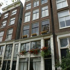 Pand met gevel onder gesneden rechte lijst met triglyfen en consoles, met geblokte pui en omlopende puilijst