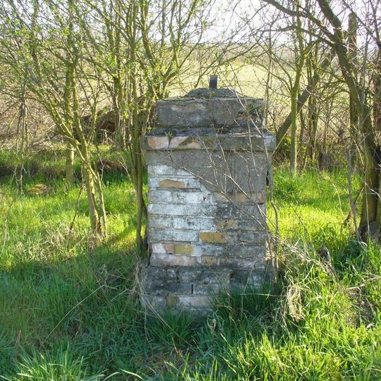 Podstavec s ulomeným kovovým křížem u silnice z Malíče