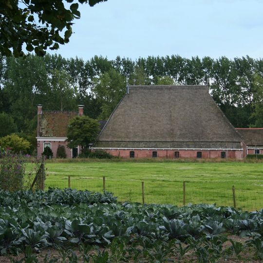 Kop-hals-rompboerderij zadeldak met schoorstenen en borden en met stal onder hoog met pannen belegd schilddak