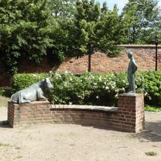 Liegende Kuh und stehender Mensch, aus Metall, auf Steinsockel