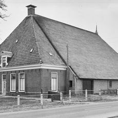 Grote stelboerderij met vier smalle vensters, dakkapel, zeer hoog voorschild, dakkapel en met riet gedekt schuurdak