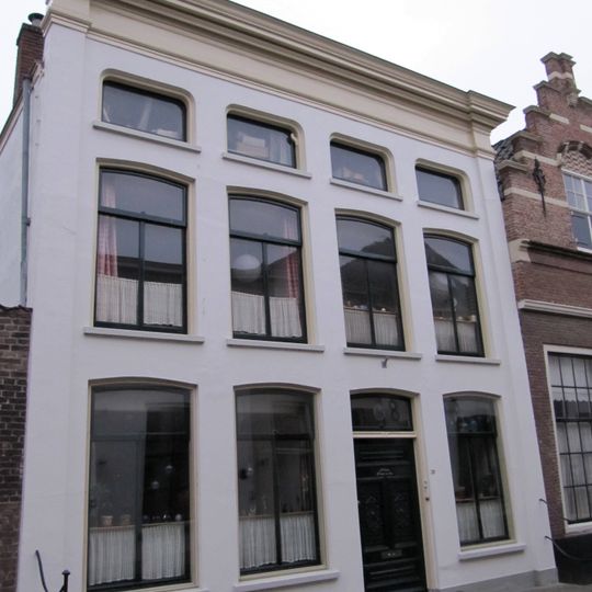 Pand, bestaande uit twee huizen onder schilddaken, in het derde kwart 19e eeuw samengetrokken achter een gepleisterde lijstgevel ter breedte van vier vensterassen