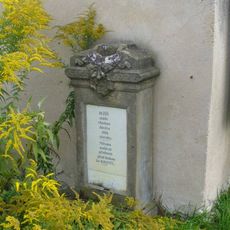 Podstavec s vylomeným křížem u zdi farní zahrady v Počaplech