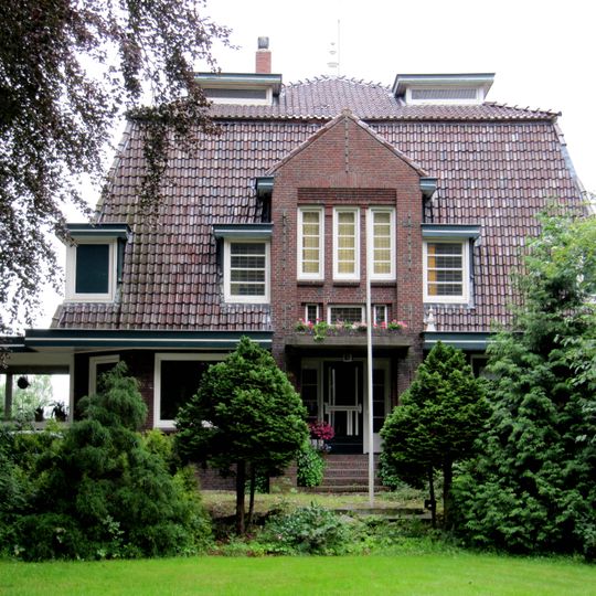 Dwarshuis met omlijste ingang en forse kroonlijst onder schilddak met hoekschoorstenen met borden