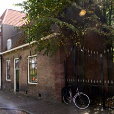 Pand met verdieping en schilddak. Deur met snijwerk, bovenlicht en pilasteromlijsting met hoofdgestel. Houten kroonlijst