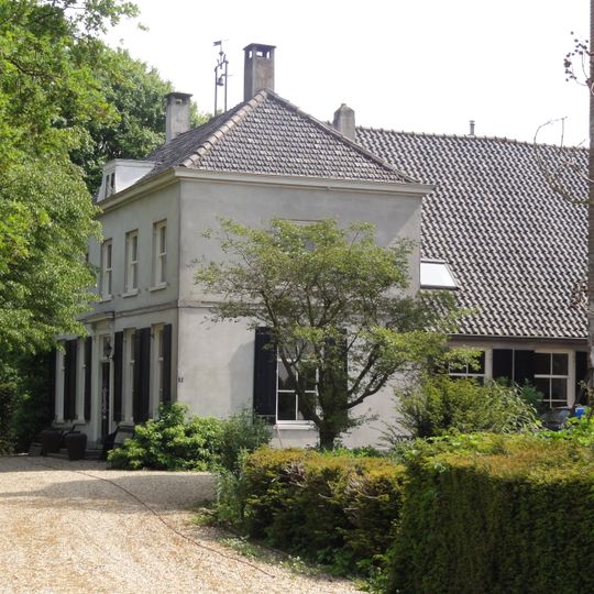 Gepleisterde boerderij op T-vormige plattegrond, naast de poorttoren van Poelwijk. Deuromlijsting met consoles onder het hoofdgestel en bovenlicht met levensboom