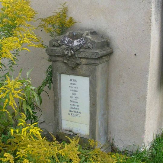 Podstavec s vylomeným křížem u zdi farní zahrady v Počaplech