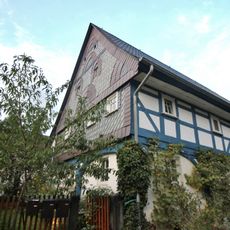 Wohnstallhaus mit Oberlaube, Remisenanbau mit zwei großen Toren und Scheune im rechten Winkel, weiteres Wohnstallhaus in der Flucht der Scheune und südliches Wohnstallhaus sowie Granitzaunspfosten der Nutzgarteneinfriedung Kumschütz 8