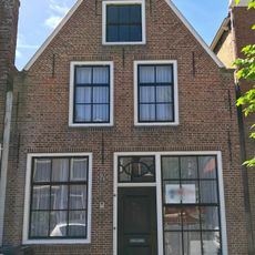 Pand met deur met kussenpanelen onder zadeldak tegen puntgevel