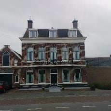 Herenhuis met aangrenzend koetshuis, onder invloed van het neo-classicisme. Het pand is gebouwd tegen een dijk; aan de achterzijde is de kelderverdieping zichtbaar