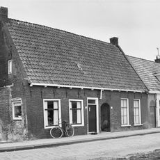 Hofje met hoofdgebouw onder zadeldak evenwijdig aan de straat tussen twee topgevels (vormt een geheel met nr. 33)