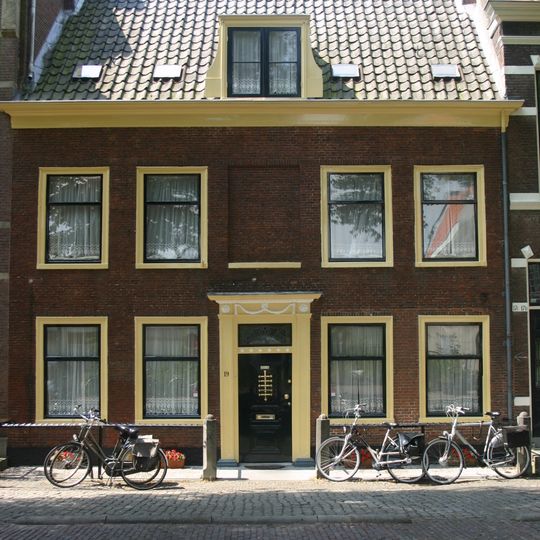 Pand met brede gevel met rechte kroonlijst. Zadeldak over lengte der gevel. Gesneden Louis Seize deuromlijsting