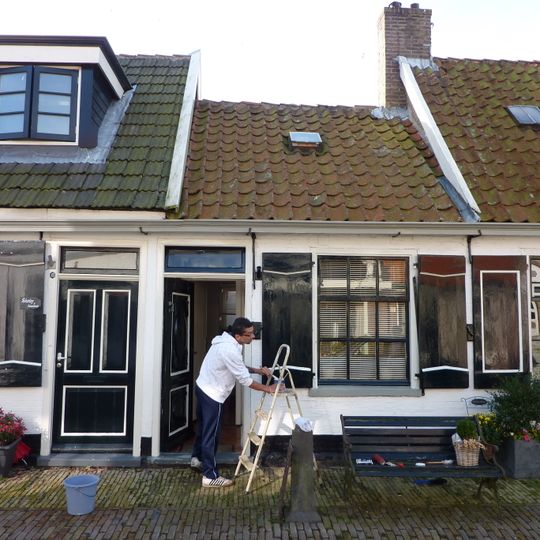 Klein huisje onder een dwars dak met de nummers 8 en 12. Aardige details aan vensters. Luiken en goede deur. Achterschot