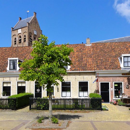 Panden onder lang zadeldak tussen topgevels met aan de westzijde een poortdoorgang naar het kerkhof