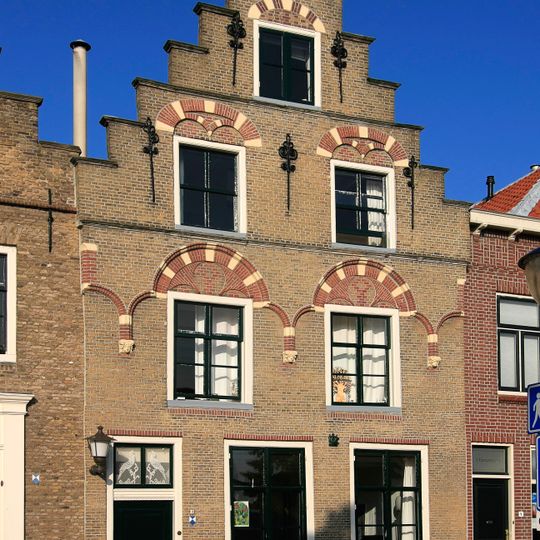 Pand met trapgevel van het Dordtse type met geblokte ontlastingsbogen, in de verdieping rutend op muurstijlen op Jonische kapiteeltjes met koppen tussen de vensters.