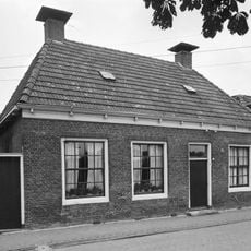 Woning met drie zestienruitsvensters onder schilddak met hoekschoorstenen met borden