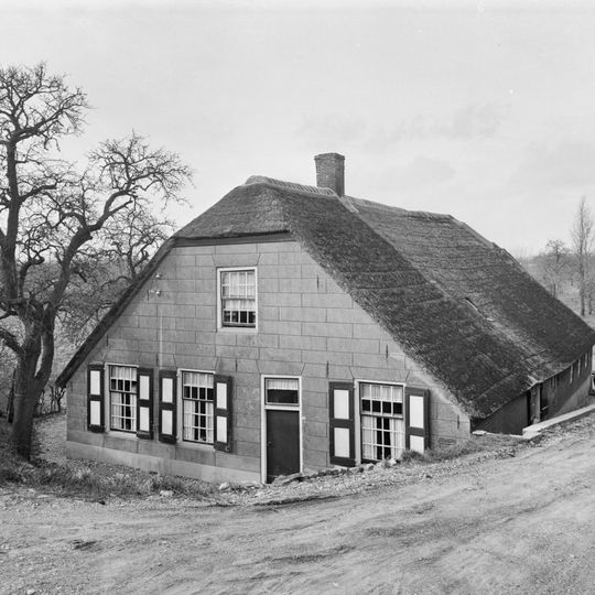 Boerderij, onder rieten wolfdak. In de gepleisterde voorgevel vensters met luiken en 20- en 16-ruitsschuiframen