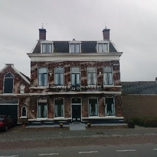 Herenhuis met aangrenzend koetshuis, onder invloed van het neo-classicisme. Het pand is gebouwd tegen een dijk; aan de achterzijde is de kelderverdieping zichtbaar