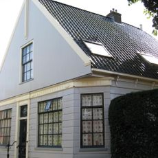 Houten dijkhuis met puntgevel, onderpui met fries in empirestijl, overhoeks geplaatst raam