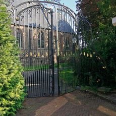 Nederlands Hervormde Kerk: smeedijzeren toegangshek, uitgevoerd in Lodewijk XV-stijl, met gebogen zijstukken en top, versierd met voluten en rocaillemotieven, deels verguld