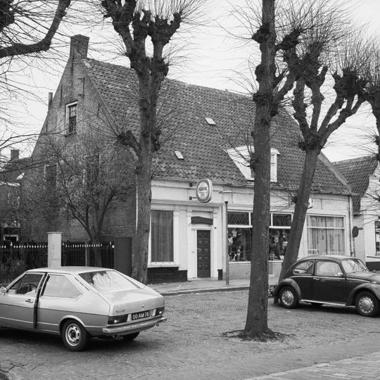 Dwarshuis zonder verdieping onder hoog zadeldak, met pannen gedekt dat aan de korte zijden wordt afgesloten door puntgevels met vlechtingen