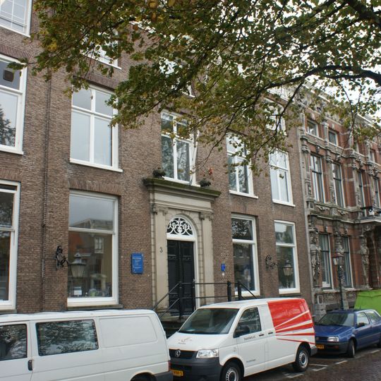 Breed statig patriciershuis, hoge stoep hardstenen ingangsomlijsting, lantaarn, rechte kroonlijst met metopen en grove consoles, vooruitspringende middenrisaliet