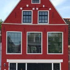 Pand onder zadeldak tegen puntgevel met waterlijst en in de top twee vensters onder geblokte bogen