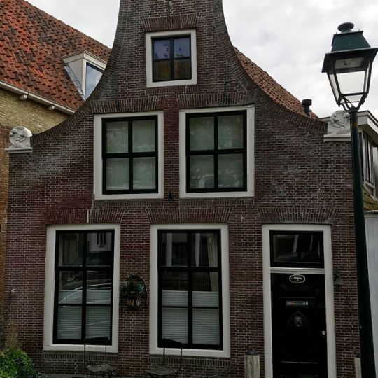 Hoekpand onder zadeldak tegen klokgevel met aanzetkrullen en driezijdig fronton