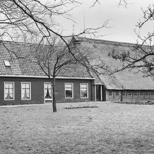Boerderij met in het midden onderkelderd lange voorhuis en voortopgevel met waterlijst waarboven twee kleine vensters en topschoorstenen met borden