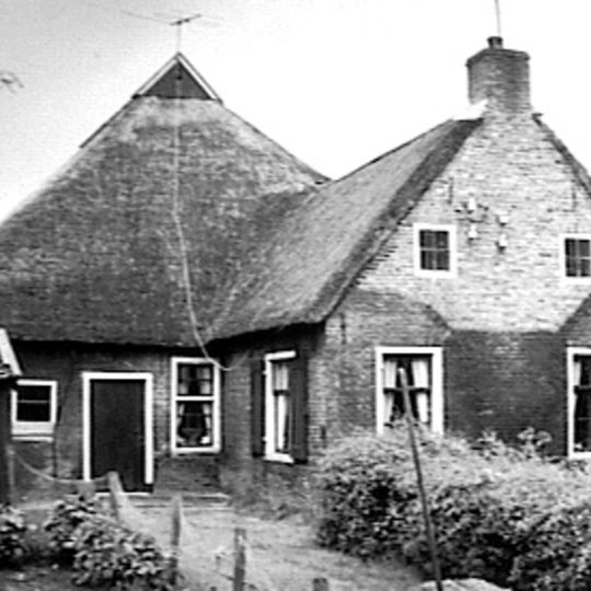 Kop-rompboerderijtje in roodbruine handvormsteen met staafankers onder rieten zadeldak met vorstpannen met topschoorsteen