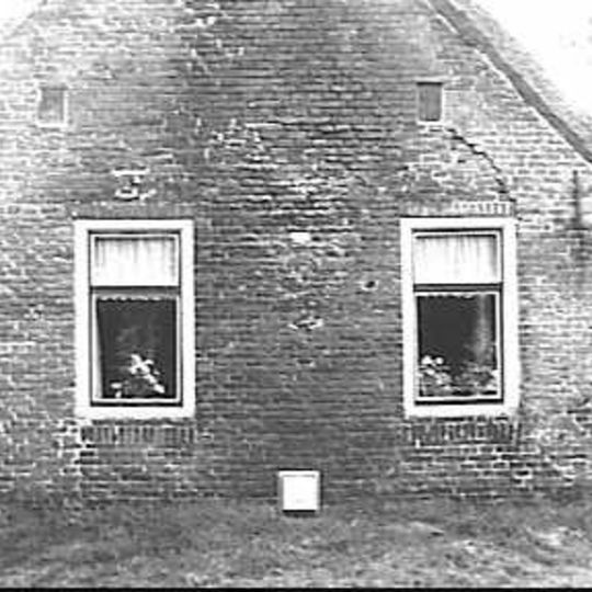 Arbeiderswoning in roodbruine handvormsteen onder driezijdig rieten schilddak met uilebord en makelaar tegen rechte voorgevel met topschoorsteen met bord