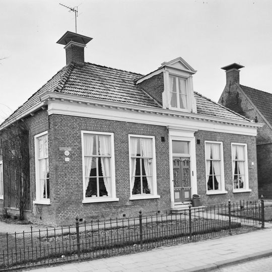 Woonhuis met zesruitsvensters en geblokte kroonlijst onder laag schilddak met dakkapel en hoekschoorstenen met borden