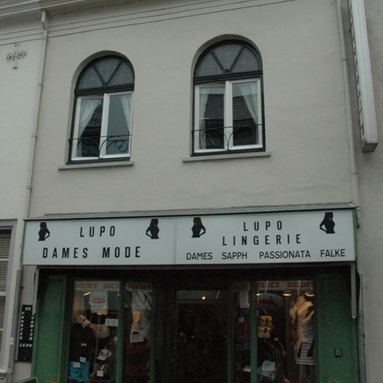 Dubbelbeukig gebouw, voorzien van een gepleisterde rechte gevel aan de straat en een zadeldak tussen zij-tuitgevels met vlechtingen