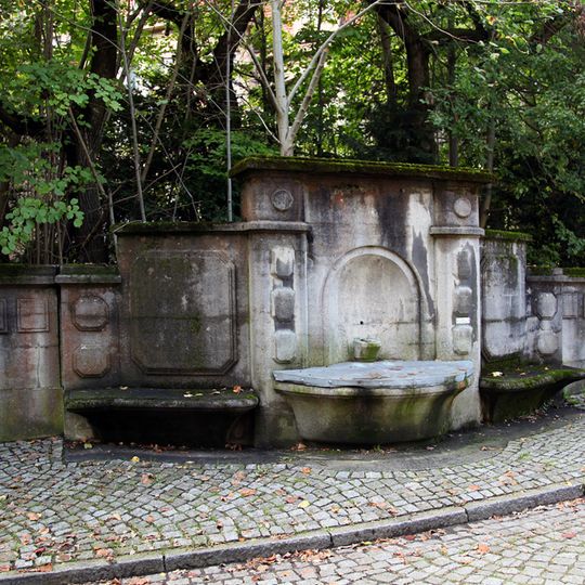 Wandbrunnen in Einfriedungsmauer mit Wasserbecken, Bronze-Figur in Nische und seitlich je einer flankierenden Steinbank Hufelandstraße 15