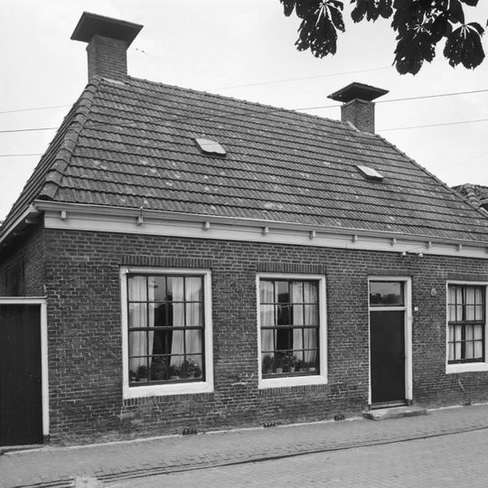 Woning met drie zestienruitsvensters onder schilddak met hoekschoorstenen met borden